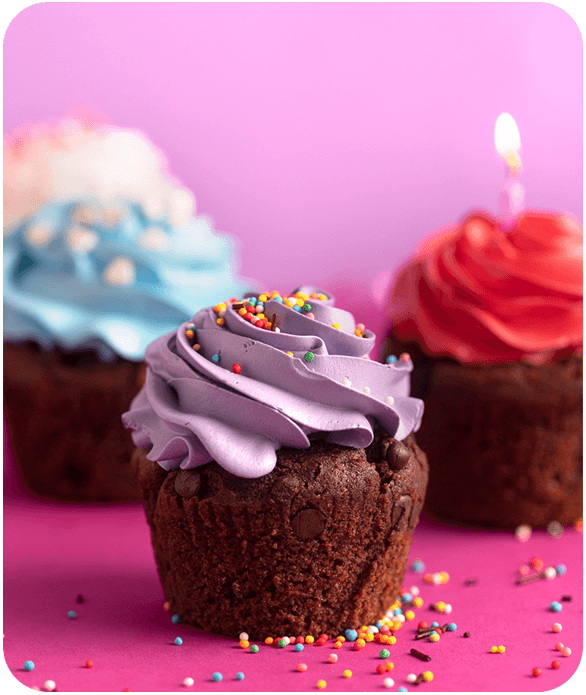 Cupcake de chocolate con glaseado morado en primer plano con cupcakes glaseado azul y rojo al fondo